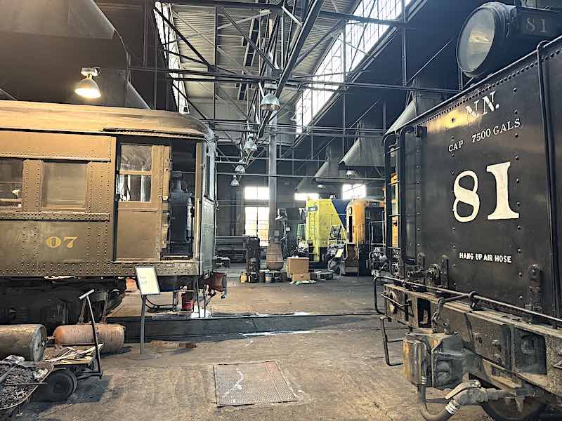 A passenger coach and steam engine being restored in the Northern Nevada Railway Museum’s machine shop and engine house